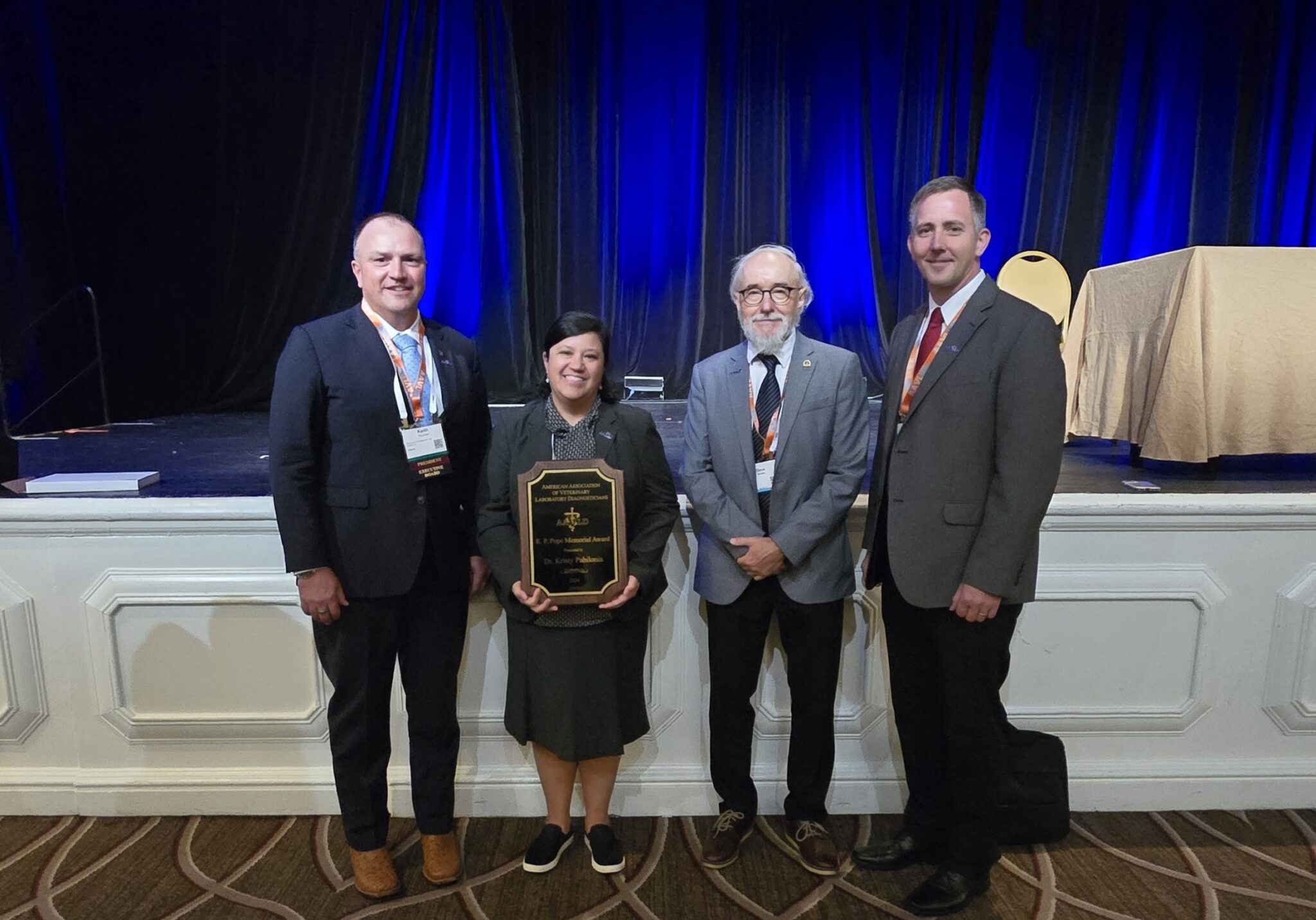 a group of people smile for a picture, a woman in the middle holds an award