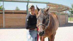 a person holds a brown horse by the reigns smiling at the camera