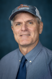 a portrait of a man with a blue shirt and hat, blue tie, and blue background