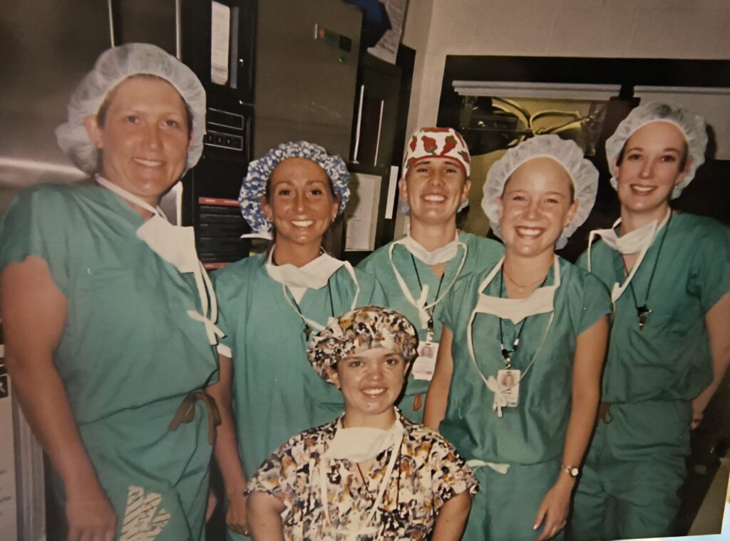 a group of veterinary professionals in teal scrubs smile for the camera, wearing hair nets and surgical masks off their faces