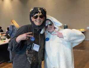 Two individuals wearing animal-themed costumes, one resembling an insect and the other resembling a sheep, posing together indoors during a themed event.