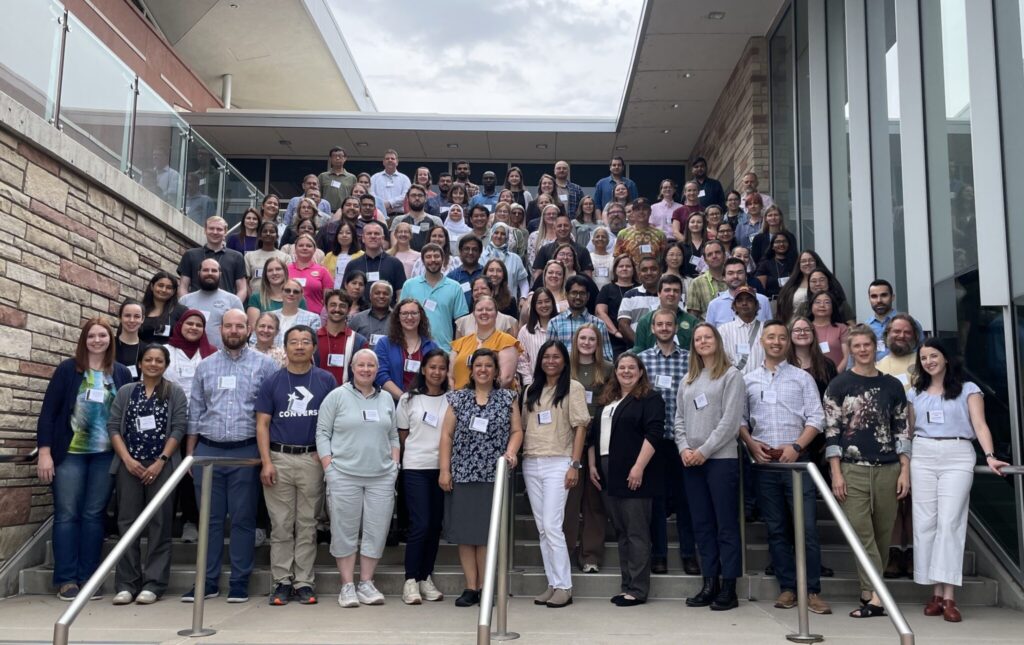 Large group photo of event participants standing on outdoor steps in front of a building, gathered for a group picture during the symposium.
