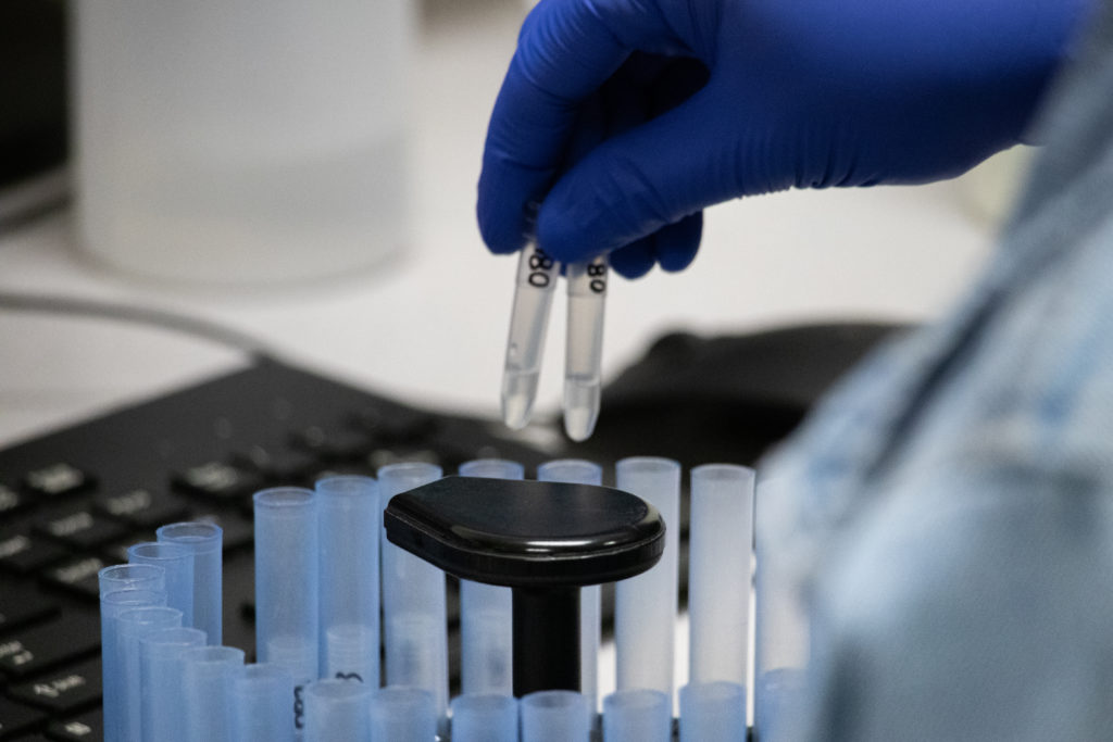 gloved hand placing test tubes into centrifuge