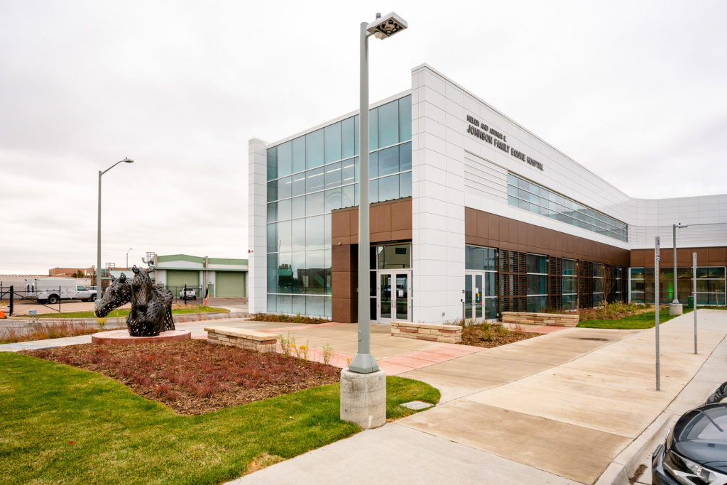 A modern white and glass veterinary medical building is shown with a horse statue in the landscaped front area.