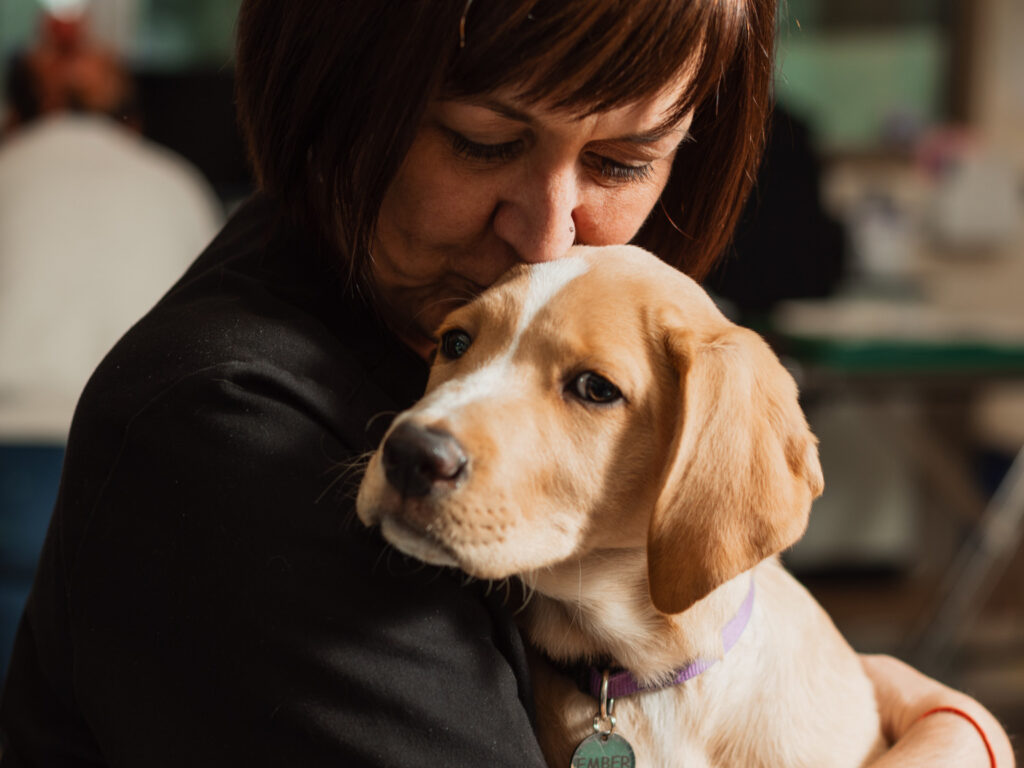 woman kissing the head of a puppy while holding it in her lap