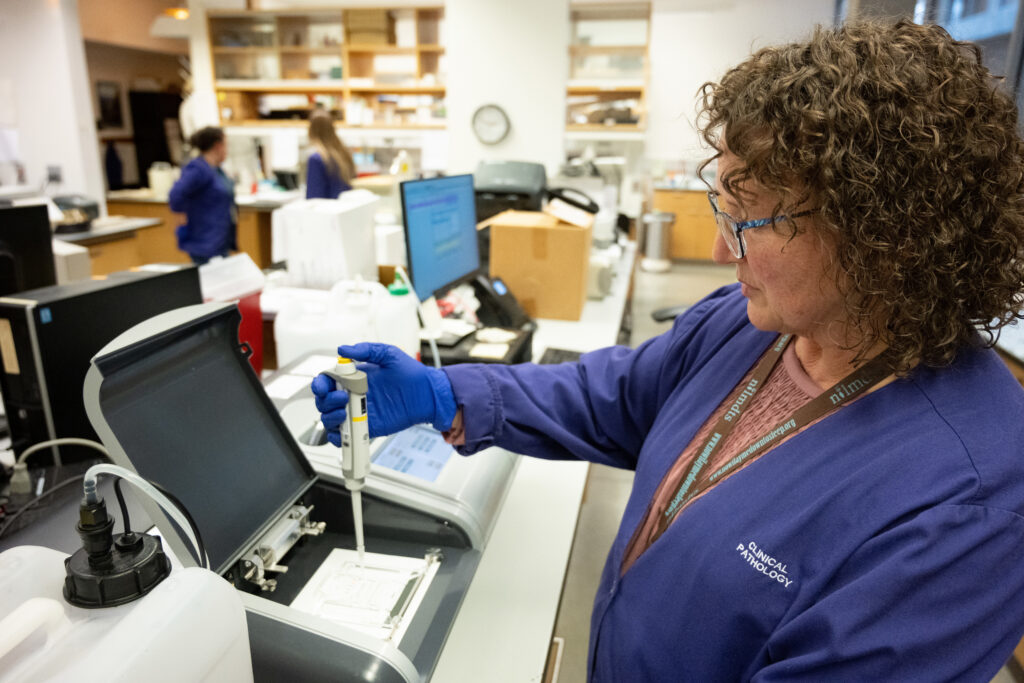 A person in a lab uses a pipette at a workstation with diagnostic equipment in a clinical laboratory.