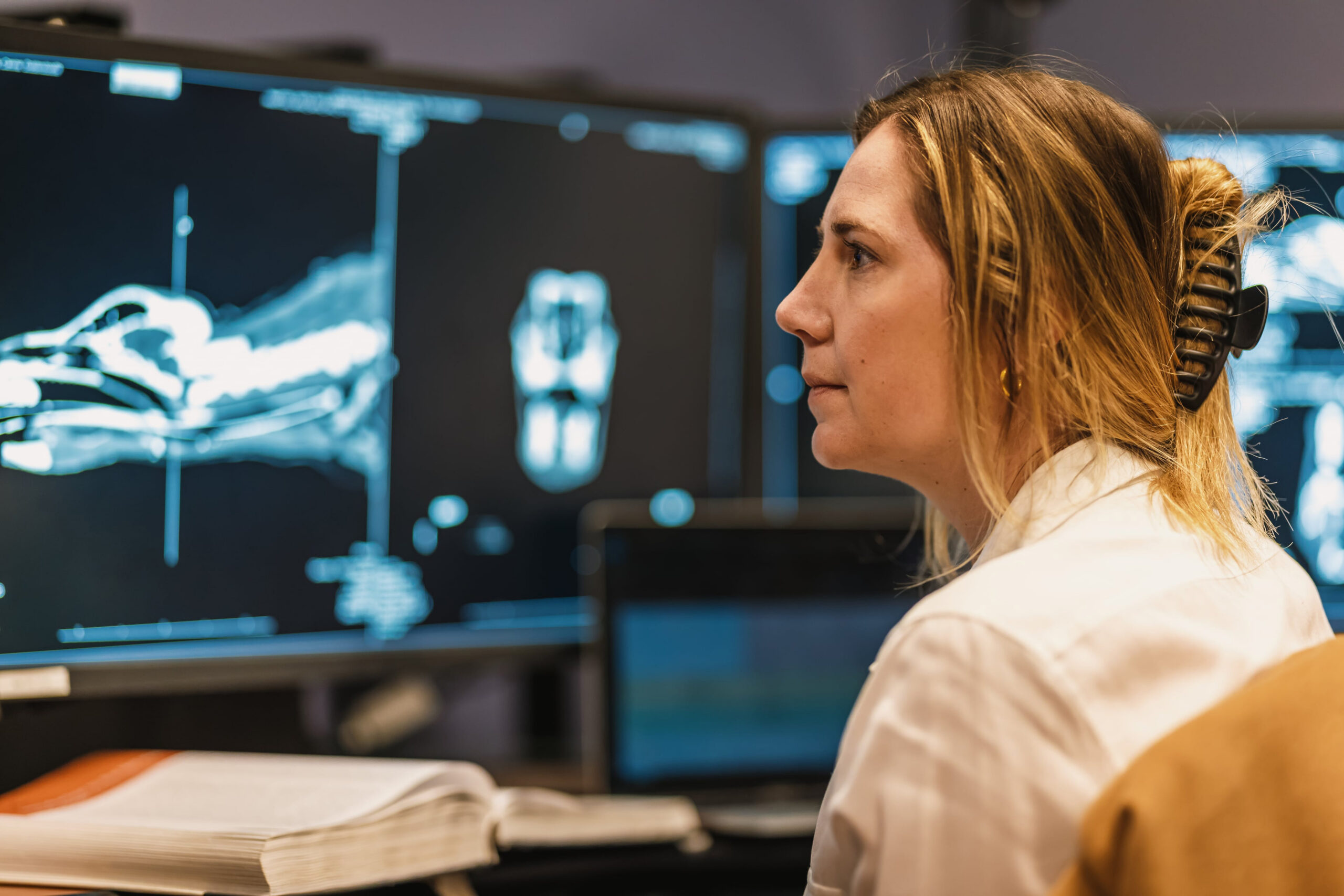 A person in a white coat reviews diagnostic images displayed on large computer monitors.