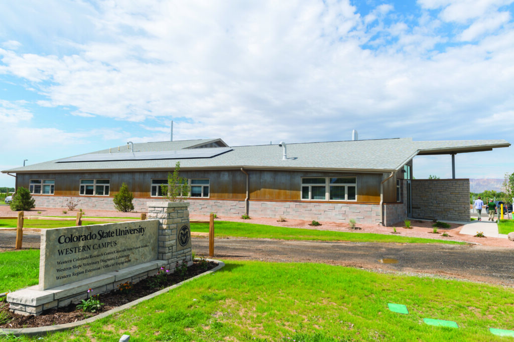 A Colorado State University Western Campus building stands behind a stone entrance sign on a grassy landscape under a partly cloudy sky.