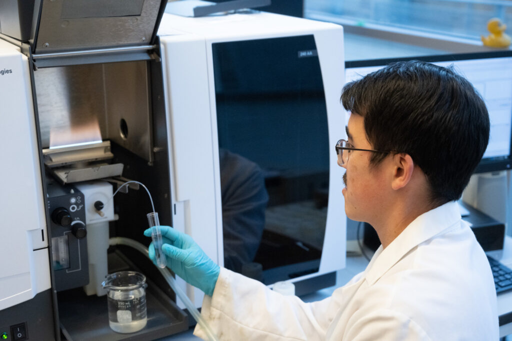man wearing lab coat and gloves holding test tube in front of diagnostic machine