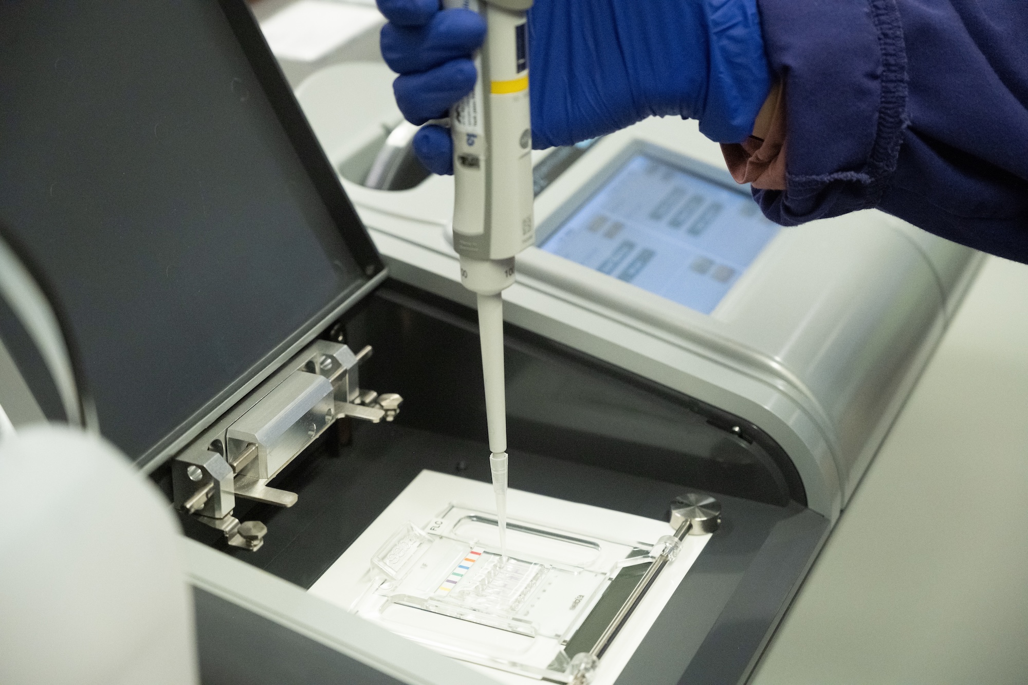 gloved hand holding pipette over diagnostic machine
